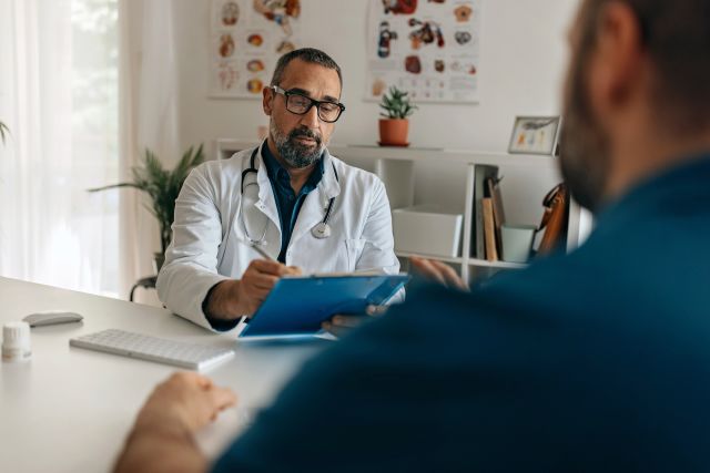 View of a surgeon writing in a chart, facing his patient answering questions