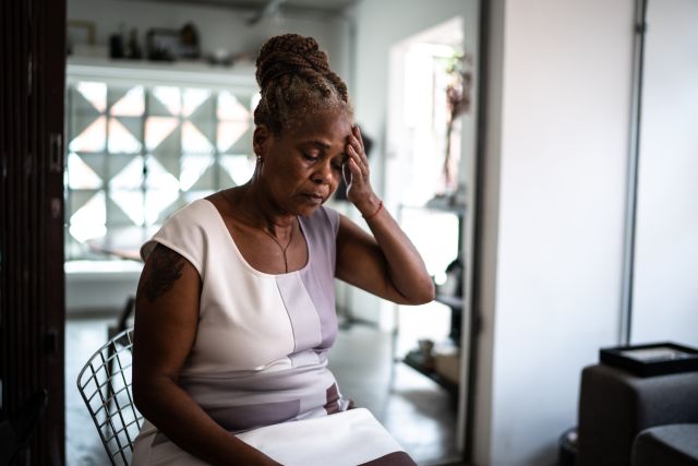 A woman with thyroid fatigue sits in her kitchen with her head down and eyes closed, struggling because she is tired