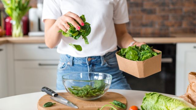 unidentifiable woman dropping greens into glass bowl in a kitchen