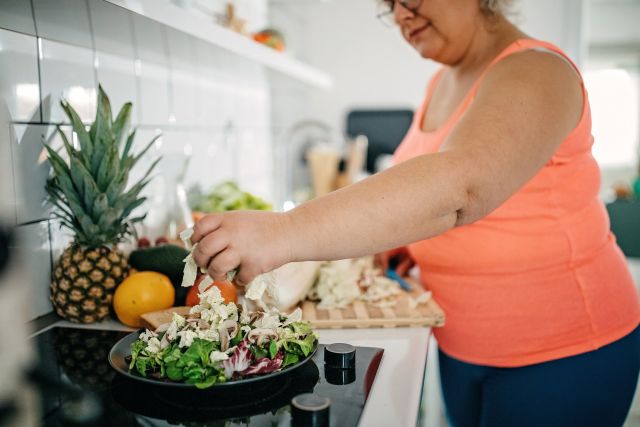 woman in a kitchen preparing a big plate of a whole foods salad 