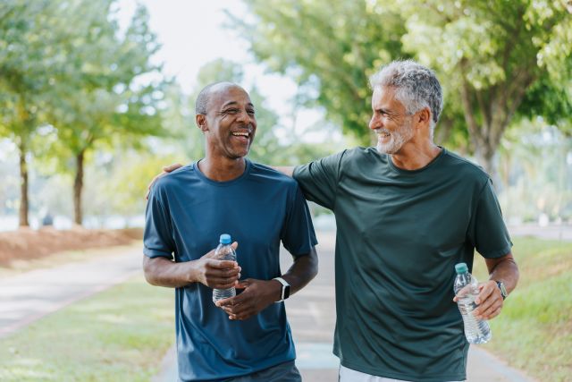 a pair of fit middle aged men, one Black, one white, laugh and enjoy one another's company after exercising outside in the park