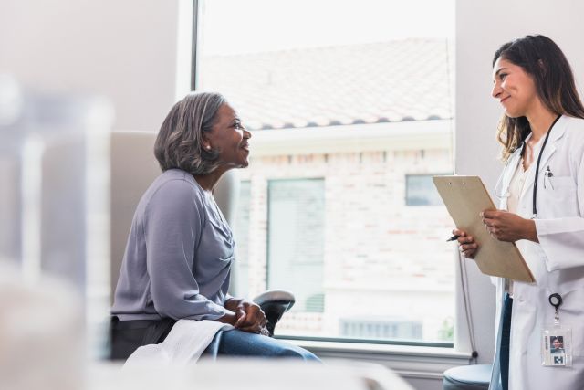 A caring female doctor smiles with compassion while talking with a senior female patient during a medical exam for psoriasis