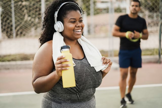 Smiling plus size woman in athletic clothing wearing headphones wearing headphones outside