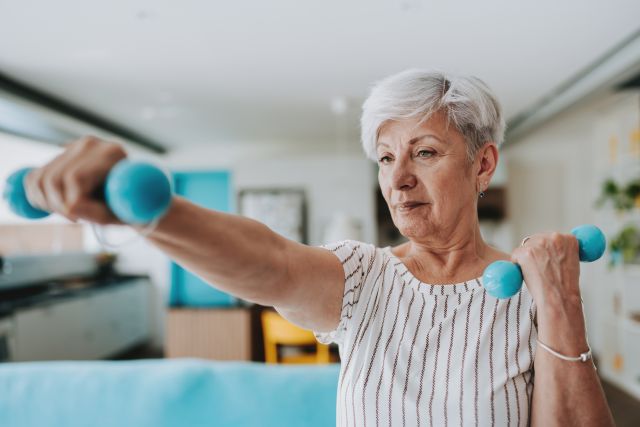 an older Hispanic woman uses light dumbbells to exercise and help keep her bones in shape