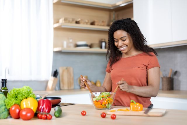 A young Black woman prepares a salad featuring vibrant healthy vegetables that contribute to healthy, glowing skin