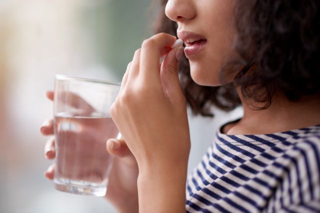 Cropped shot of an unrecognizable teenage girl taking adhd medication with a glass of water