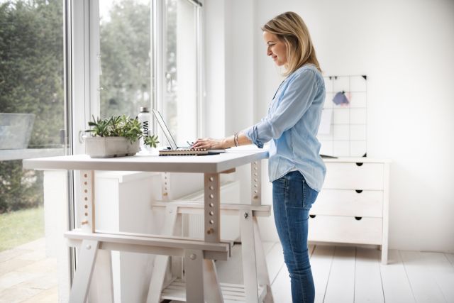a middle aged blonde white woman stands at her standing desk, displaying good posture