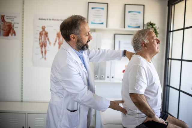 An oncologist examines a senior man experiencing back pain. Metastatic uveal melanoma can cause a wide range of symptoms depending on where it has spread.