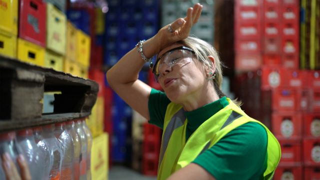 A female warehouse worker experiences a hot flash at work. Known as vasomotor symptoms, hot flashes and night sweats are the most common symptom of perimenopause.