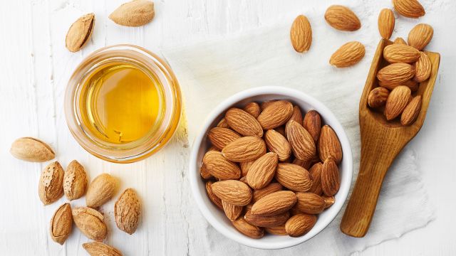A container of almonds next to a jar full of almond oil.