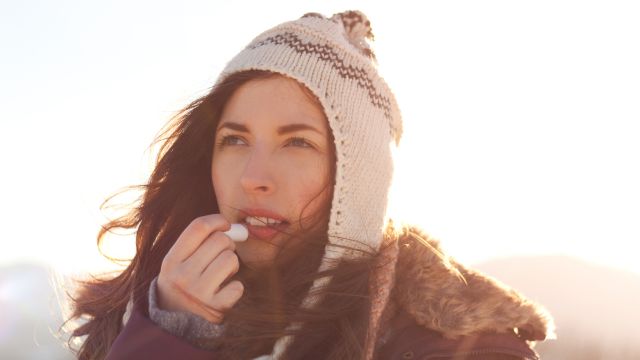 A woman applying chapstick to her lips in the cold.