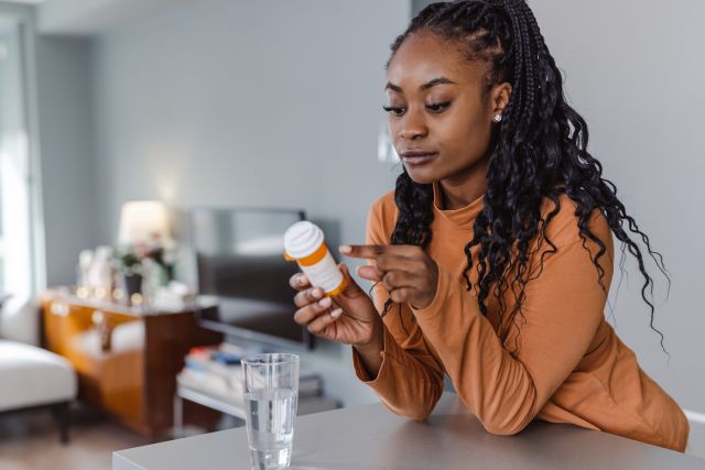 A young woman reads the label on a prescription medication. Following dosing instructions carefully is essential to getting the most benefit from any migraine therapy.