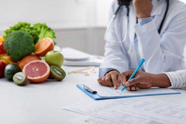 close up of the hands of two healthcare providers writing a nutrition plan with fruits and vegetables on the side