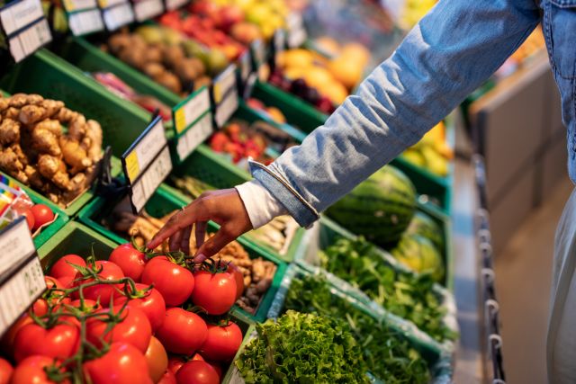 a hand reaches out to pick some tomatoes from the produce aisle at a supermarket