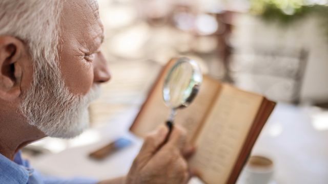A senior man uses a magnifying glass to read. Low vision aids like magnifiers can be useful for people who have impaired vision caused by age-related macular degeneration.