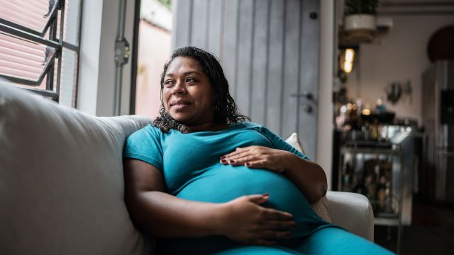 Happy pregnant woman holds her belly while looking out of a bright window