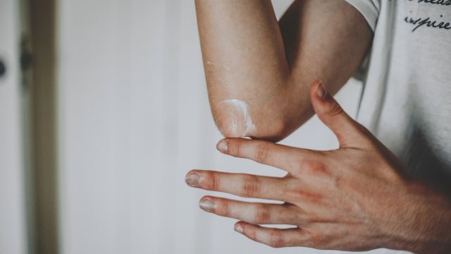 A young man applies a topical therapy to his elbow as part of a daily psoriasis management routine.