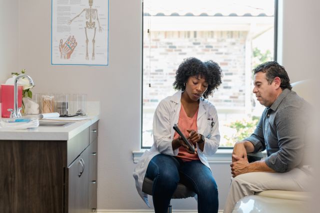 a white male patient speaks with his doctor, a young Black woman, about getting a knee replacement surgery for his knee arthritis