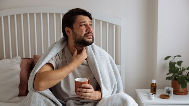 Man with the flu sitting up in bed drinking hot tea