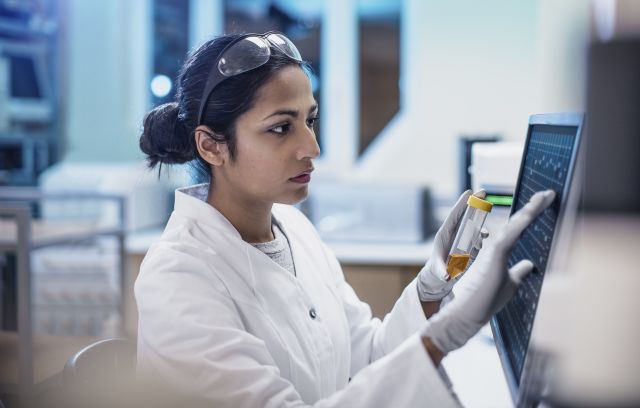 A female research scientist with dark hair conducts research into a new breast cancer vaccine using a touch screen computer.