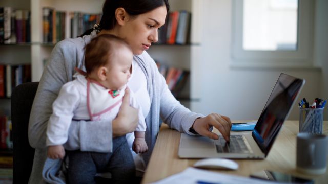 A mother holds her infant child as she researches primary immunodeficiency on a laptop computer.