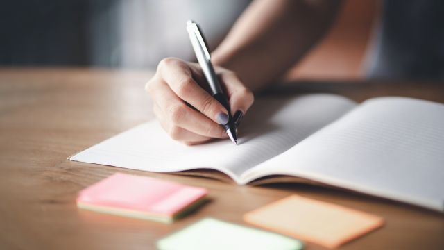 A closeup image of a woman's hand writing in a journal. Many people keep a headache diary with a paper and pen, others prefer electronic documents or apps.