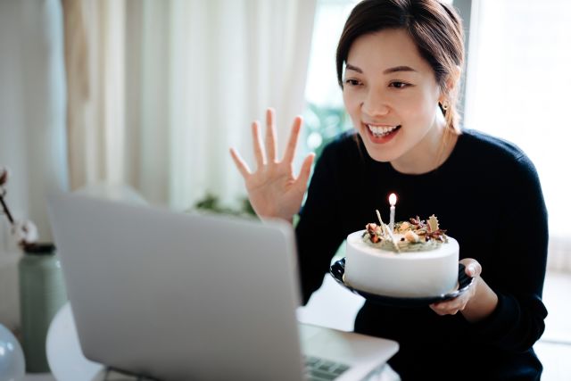 a young Asian woman celebrates a holiday with a cake via videoconference with her loved ones