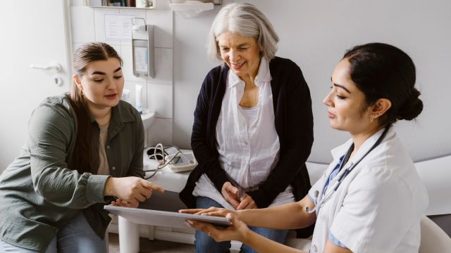 A senior woman and her adult daughter speak with a healthcare provider about a newly-prescribed treatment for Parkinson's disease.