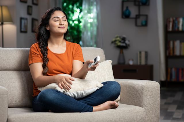 a young Middle Eastern woman smiles with her eyes closed as she sits in her living room breathing clean fresh air