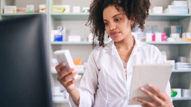 A pharmacist reviews information for a patient assistance program while filling a prescription.