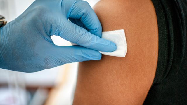 A healthcare provider cleans an area of the upper arm of a patient with an alcohol swab. The upper arm is one potential site for a subcutaneous infusion of immunoglobulin.