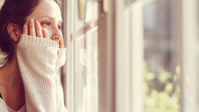A woman looks out at window as she struggles with depression symptoms.