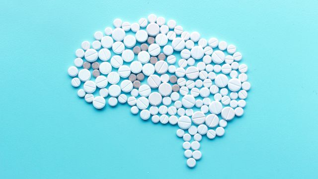 Pills are arranged in the shape of a brain on a blue background. Migraine is a neurological condition that is different than a headache.