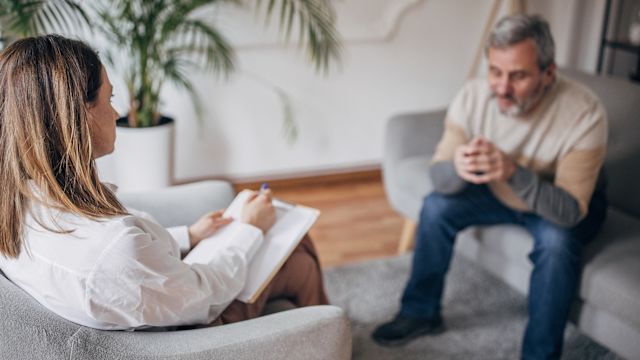 A man living with cancer speaks to a counselor. Working with a counselor is one strategy that can help a person take care of mental health while living with cancer.