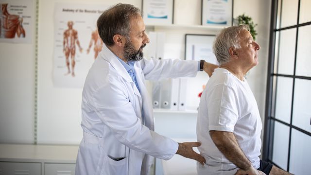 An oncologist examines a senior man experiencing back pain. Metastatic uveal melanoma can cause a wide range of symptoms depending on where it has spread.