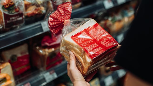 A woman reads the nutritional information and ingredients on a loaf of bread checking for allergens and additives that can cause an allergic reaction.