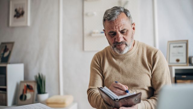 A senior man uses a pen and notepad to take notes on a recent healthcare appointment about MASLD.