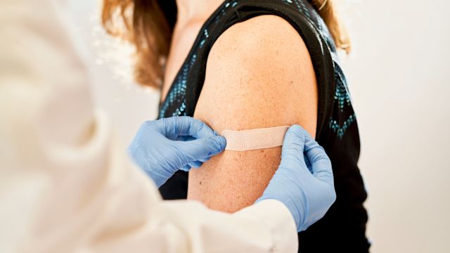 A pharmacist applies an adhesive bandage to the injection site on the arm of a female patient who has just received a COVID vaccine.