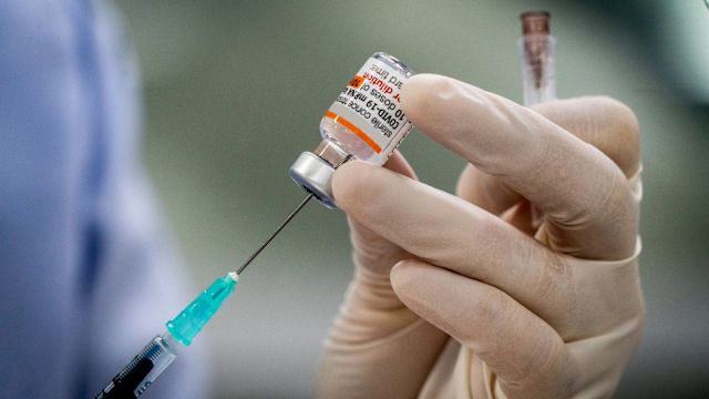 A pharmacist prepares a COVID-19 vaccine by filling a syringe from a bottle.