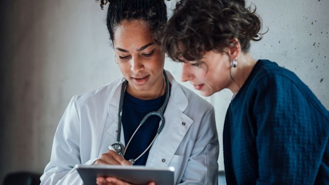 A woman and her neurologist review medication information on a tablet during an appointment to discuss epilepsy treatment.