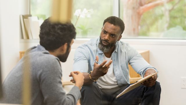 A psychiatrist talks to a young man in a healthcare office. Therapy is essential to treatment for opioid use disorder and mental health disorders.