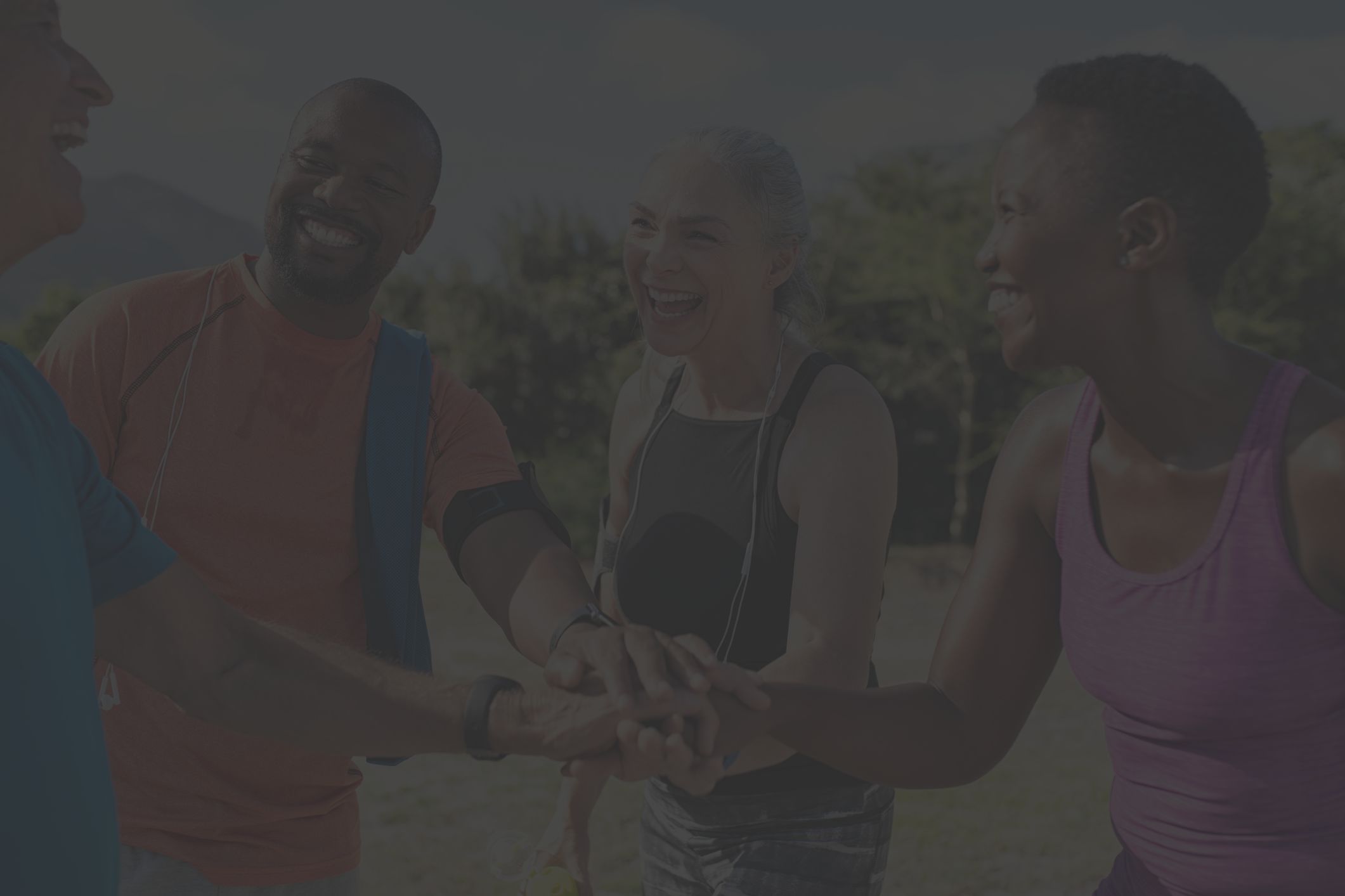 Diverse group of four people wearing colorful exercise clothes, standing in a circle and smiling while doing a group high five