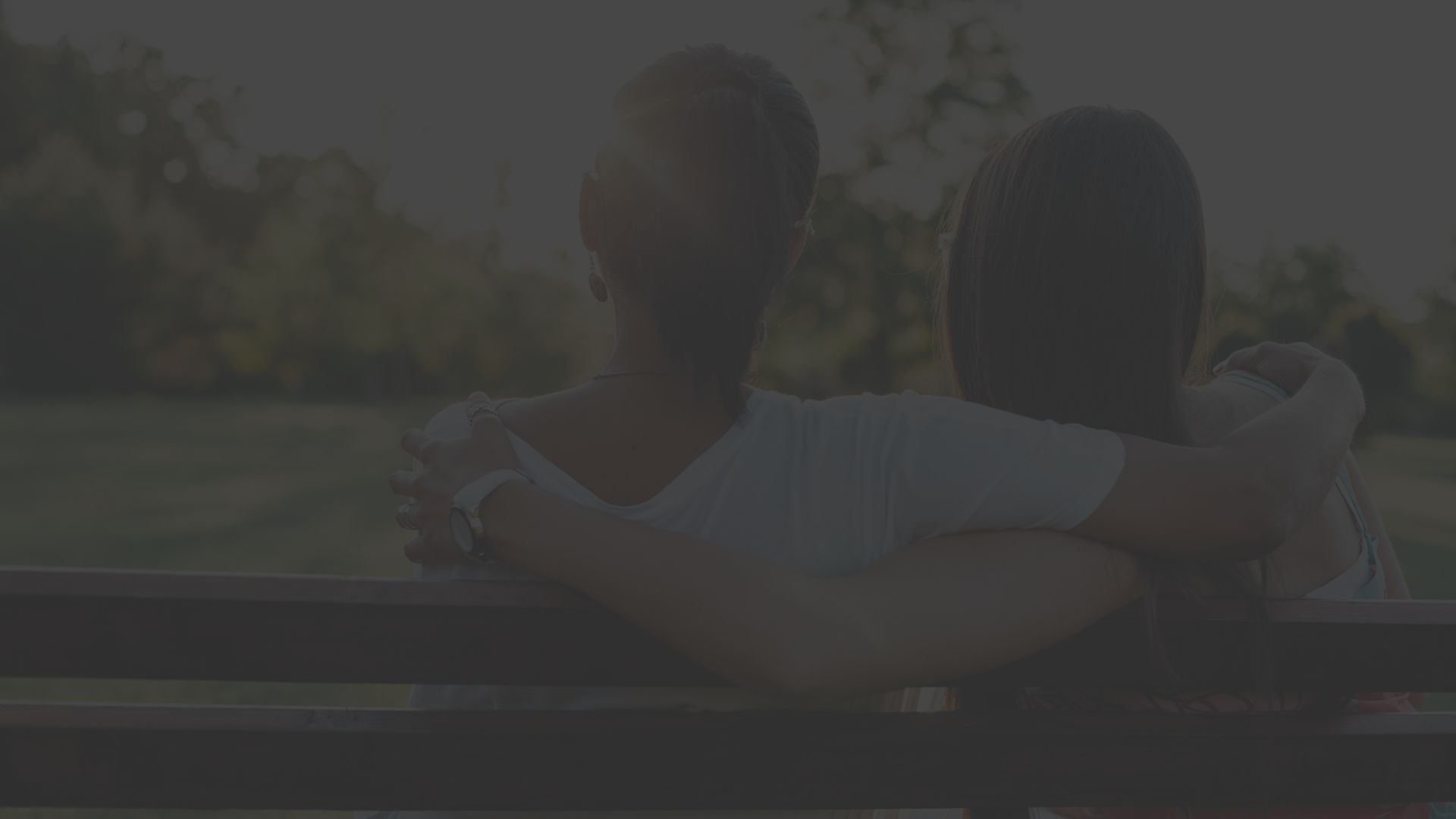 Couple snuggles on bench in park.