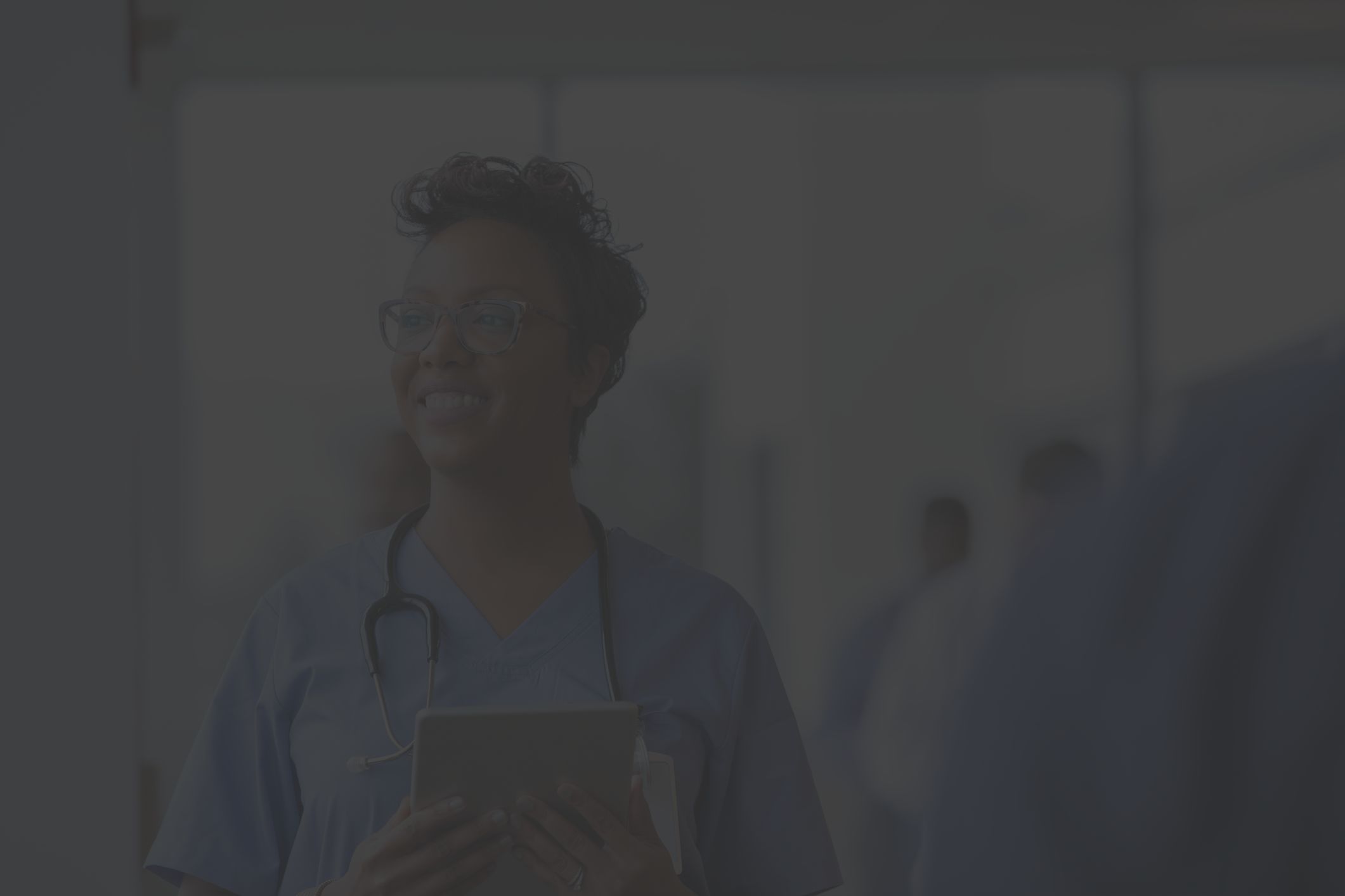 a Latina nurse in blue hospital scrubs looks up from her work tablet and smiles