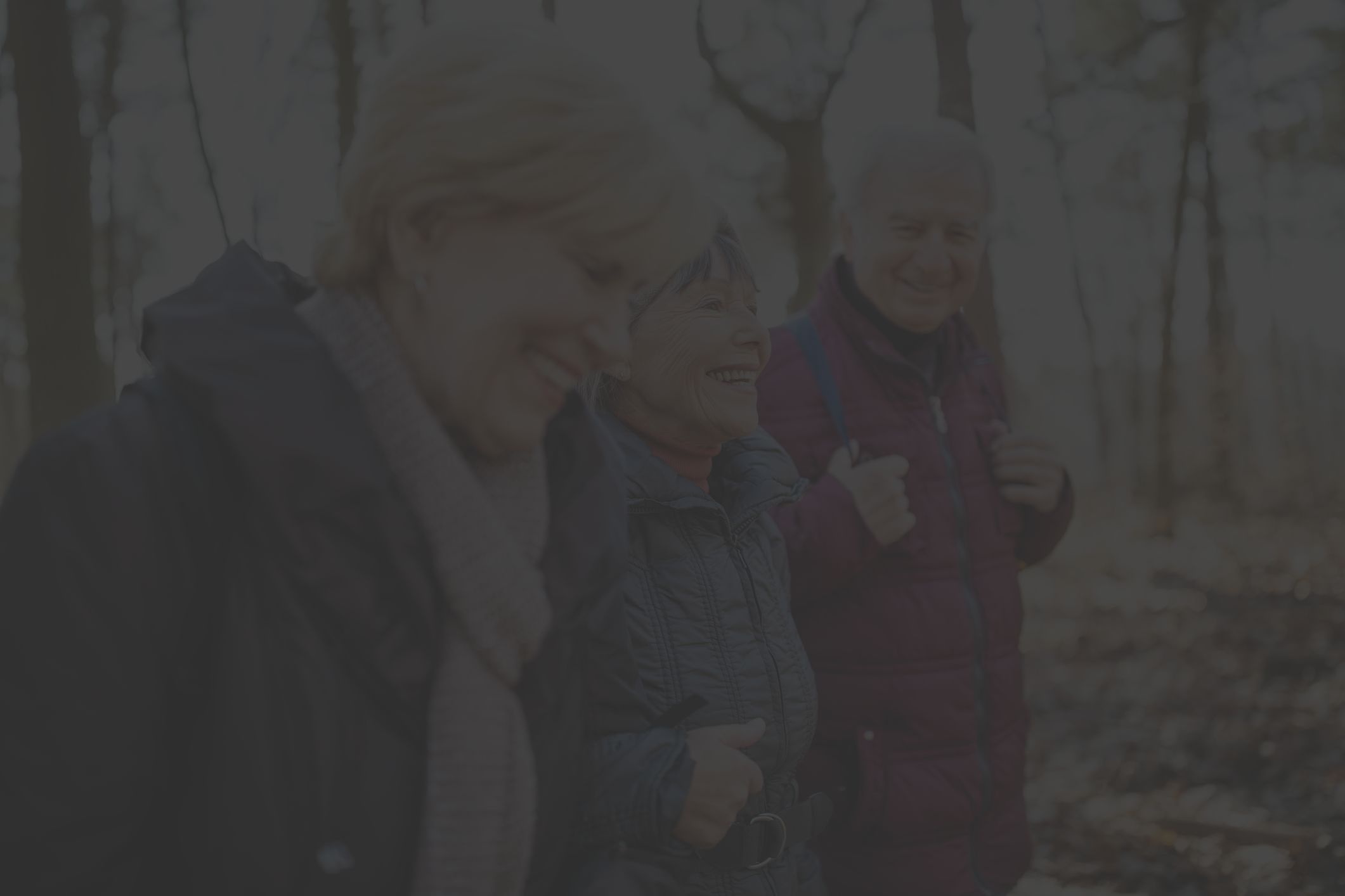 three older white adults, two women and one man, enjoy walking in the cold weather, wearing winter jackets