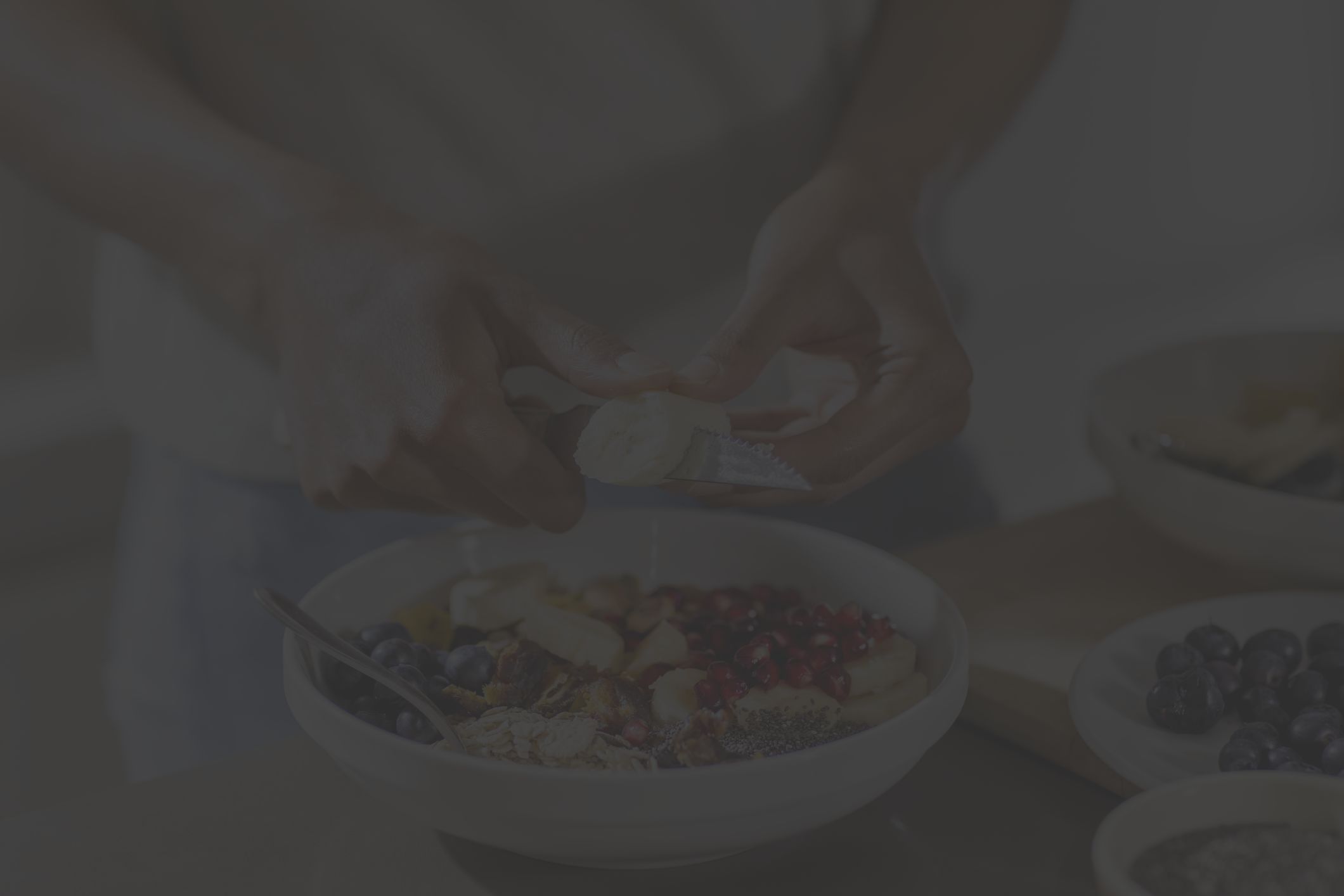 closeup of a Black woman's hands as she prepares a healthy meal of sliced fruit, granola, seeds, and berries